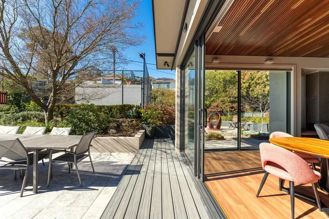 Covered deck with outdoor dining table and timber ceiling beside open sliding doors