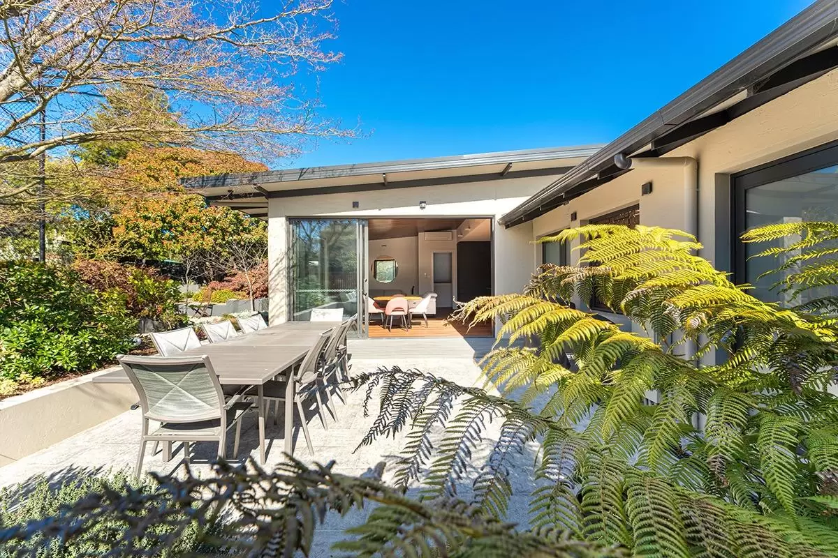 Alfresco dining table and patio framed by fern fronds with the home behind