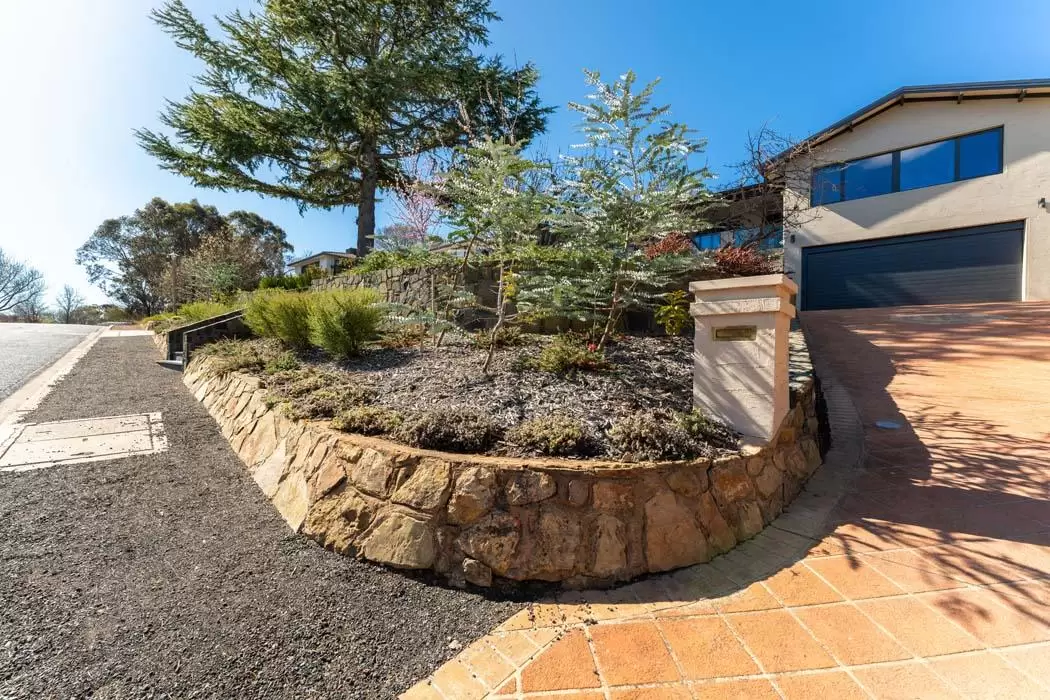 Curved sandstone retaining wall garden bed beside a gravel path and terracotta driveway