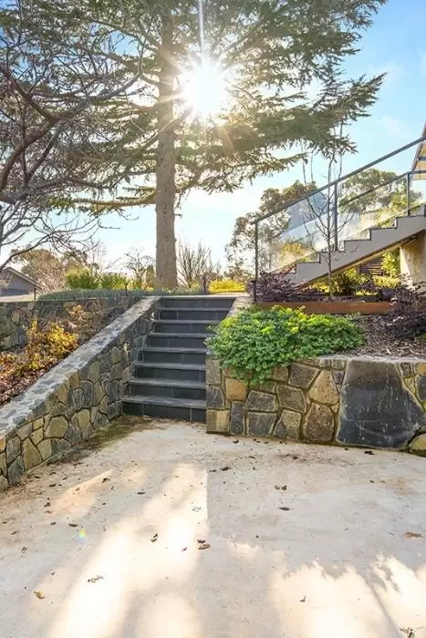Stone retaining walls and steps leading to a lower paved terrace under a mature tree