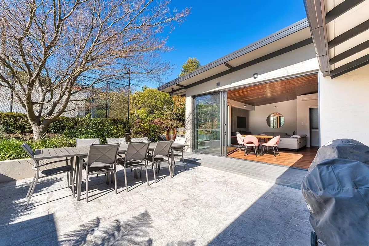 Paved patio with outdoor dining table in front of the home's open glass doors
