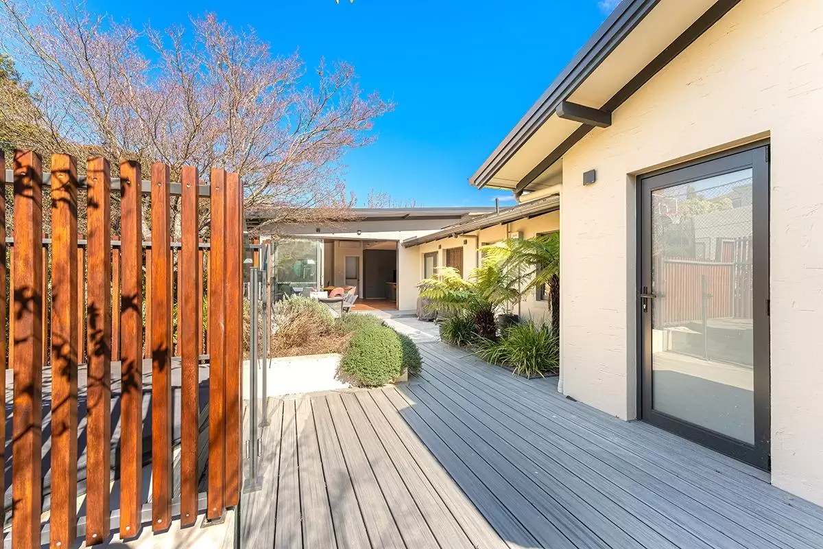 Decking path beside a timber slat screen and glass door leading to the courtyard